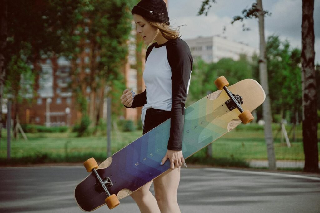 A young woman carrying a longboard skateboard in a park, enjoying her outdoor hobby.